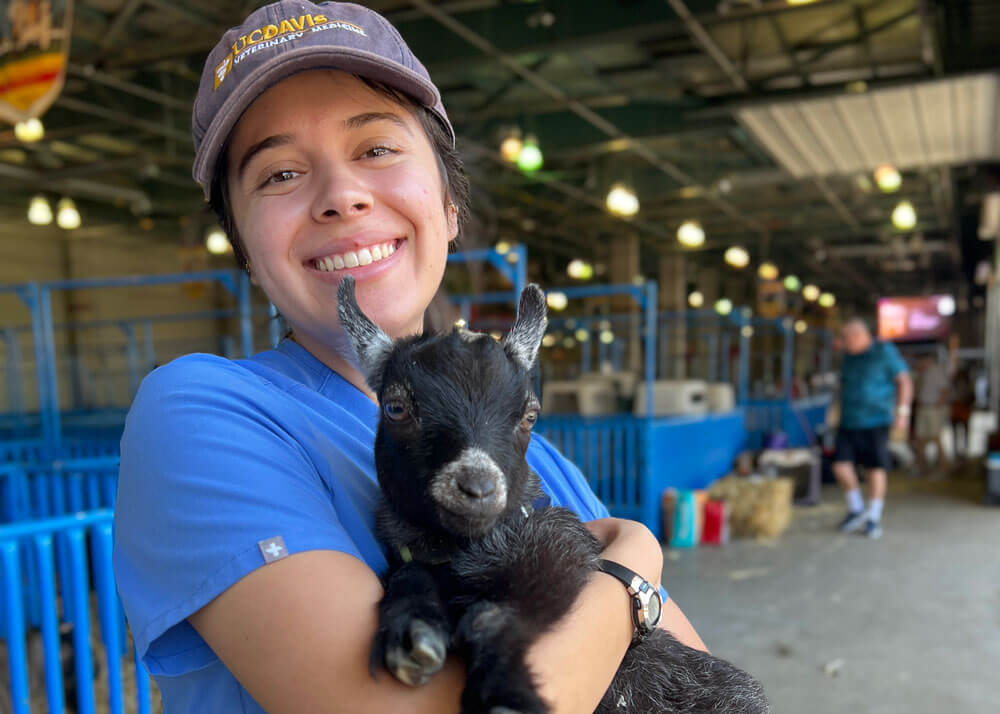 A veterinary student holding a baby goat in her arms.