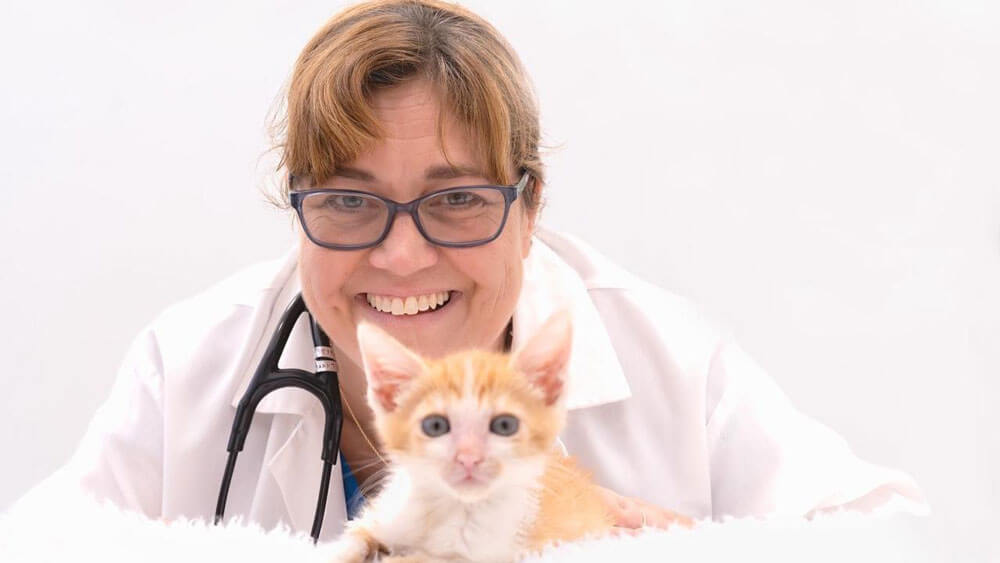 Dr. Emily McCobb smiling at the camera with a kitten in front of her.