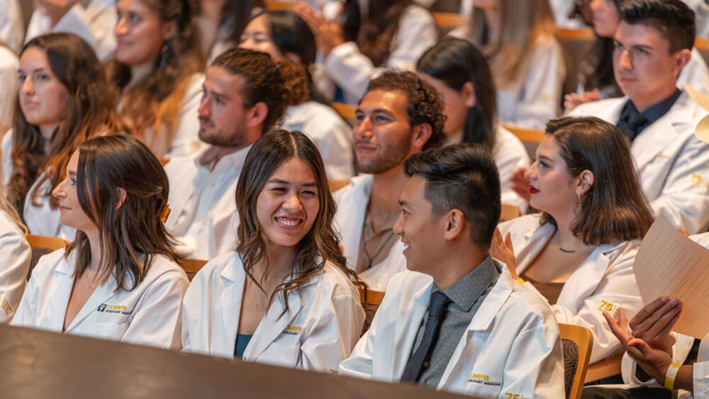 Close shot of veterinary students wearing white lab coats and sitting in an auditorium.