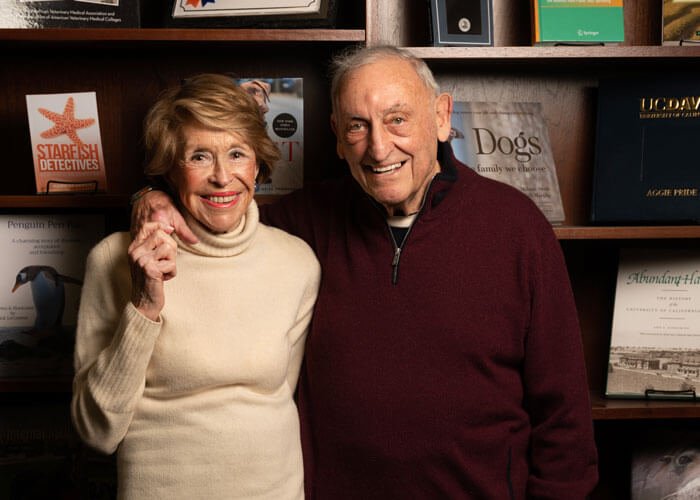 Joan and Sanford I. Weill smiling and standing next to each other in front of a large bookshelf displaying books on various animals.